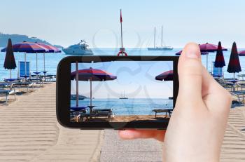travel concept - tourist taking photo of sand beach in Giardini Naxos (seaside town in Sicily) in morning on mobile gadget, Italy