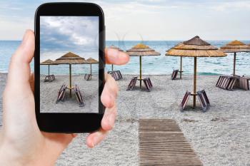 travel concept - tourist taking photo of empty Ionian sea beach in overcast day, Sicily on mobile gadget, Italy