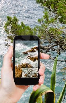 travel concept - tourist taking photo of mediterranean sea coastline in Costa Brava coast on mobile gadget, Spain