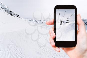 travel concept - tourist taking photo of skiing tracks and ski lift in Paradiski area, Alps, France on mobile gadget