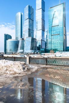 spring urban landscape with view of Moscow City and melting snow puddle