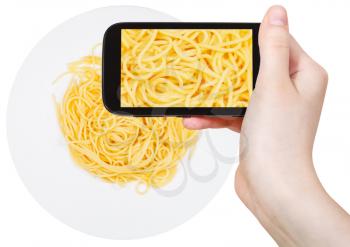 photographing food concept - tourist takes picture of italian spaghetti al burro on plate on smartphone, Italy