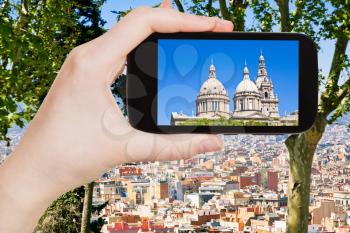 travel concept - tourist takes picture of National Art Museum of Catalonia and Barcelona skyline on smartphone, Spain