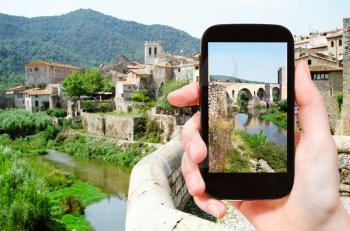 travel concept - tourist takes picture of 12th-century Romanesque bridge over the Fluvia river in Besalu town on smartphone, Spain