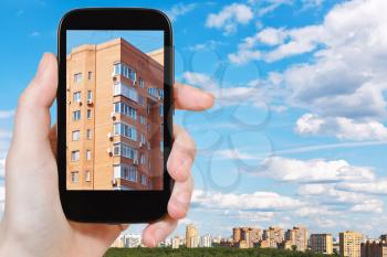 travel concept - tourist takes picture of urban appartment brick house in spring day on smartphone, Moscow, Russia