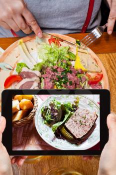photographing food concept - tourist takes picture of french meat pate on plate in restaurant on smartphone,