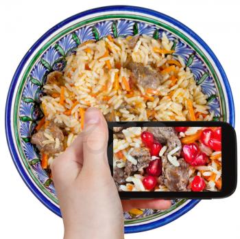 photographing food concept - tourist takes picture of asian plov with pomegranate seeds and meat on smartphone,