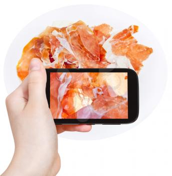 photographing food concept - tourist takes picture of sliced italian ham Prosciutto di Parma on smartphone, Italy