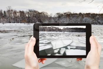 travel concept - tourist takes picture of floating of ice on river at early spring evening on smartphone, Moscow, Russia