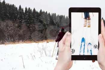 travel concept - tourist takes picture of wide cross-country skis and ski run in snow on smartphone,