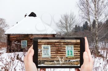 travel concept - tourist takes picture of old timbered wall of rustic house in winter on smartphone, Russia
