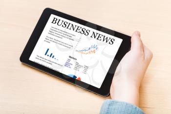 businessman hand hold tablet PC with business news on screen at office table