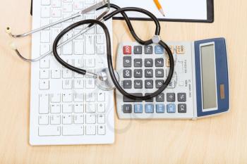 medical still life - stethoscope on white keyboard, calculator and blank clipboard
