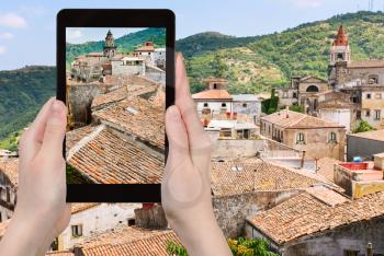travel concept - tourist takes picture of ancient tile roofs and tower of Sant Antonio church in Castiglione di Sicilia on tablet pc