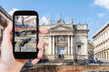 travel concept - tourist takes picture of ancient roman amphitheater (Anfiteatro Romano) and Church San Biagio in Piazza Stesicoro in Catania, Sicily on smartphone