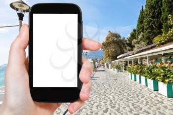 travel concept - tourist photograph Massandra street along urban beach, Yalta, Crimea on smartphone with cut out screen with blank place for advertising logo