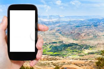 travel concept - tourist photograph Promised Land from Mount Nebo in Jordan on smartphone with cut out screen with blank place for advertising logo