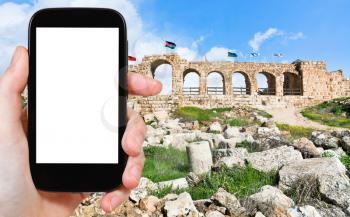 travel concept - tourist photograph the wall of Greco-Roman city of Gerasa (Jerash) in Jordan on smartphone with cut out screen with blank place for advertising logo
