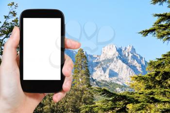 travel concept - tourist photograph Ai-Petri mountain from Alupka garden in autumn day, Crimea on smartphone with cut out screen with blank place for advertising logo