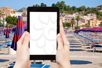travel concept - tourist photograph urban sand beach in resort town Giardini Naxos, Sicily, Italy on tablet pc with cut out screen with blank place for advertising logo