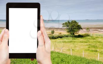 travel concept - tourist photograph green garden on sea coast in Brittany, France on tablet pc with cut out screen with blank place for advertising logo