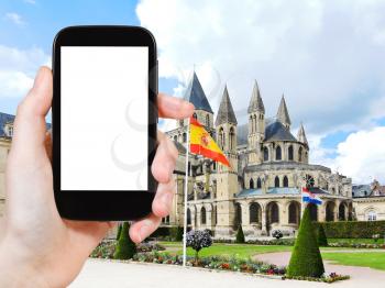travel concept - tourist photograph medieval Abbey of Saint-Etienne (Abbaye aux Hommes) in Caen city, France on smartphone with cut out screen with blank place for advertising logo