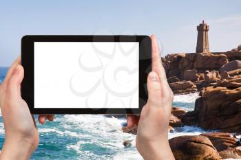 travel concept - tourist photograph lighthouse in rocks on Cote de granite rose in France on tablet pc with cut out screen with blank place for advertising logo