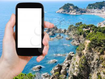 travel concept - tourist photograph town Tossa de Mar on Tossa Cape on coastline Costa Brava, Catalonia, Spain on smartphone with cut out screen with blank place for advertising logo
