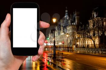 travel concept - tourist photograph Hotel de Ville (City Hall) in Paris, France at rainy night on smartphone with cut out screen with blank place for advertising logo