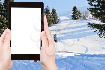 travel concept - tourist photograph skiing tracks in snow forest on mountain in Portes du Soleil region, Morzine - Avoriaz, France on tablet pc with cutout screen with blank place for advertising logo