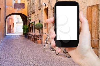 travel concept - tourist photograph old small stone medieval street in historical center of Ferrara, Italy on smartphone with cut out screen with blank place for advertising logo