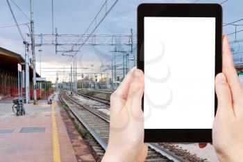 travel concept - tourist photograph the last train on railroad station in evening, Ferrara, Italy on tablet pc with cut out screen with blank place for advertising logo