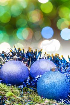 Xmas still life - blue balls, tinsel at green tree with blurred green and blue Christmas lights background