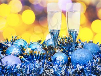 Christmas still life - two glasses of sparkling wine at blue Xmas decorations with yellow and violet blurred Christmas lights background