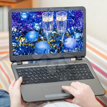 Christmas concept - man in living room touches laptop with Xmas still life on screen