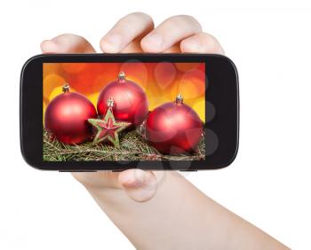 hand holds handphone with Christmas decorations on screen isolated on white background