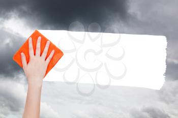 weather concept - hand deletes rainy clouds from sky by orange rag from image and white empty copy space are appearing