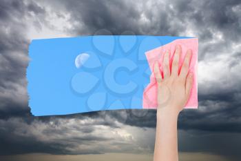 weather concept - hand deletes storm clouds by pink cloth from image and blue sky with moon is appearing