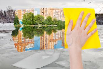 season concept - hand deletes ice block in winter river by yellow cloth from image and summer cityscape is appearing
