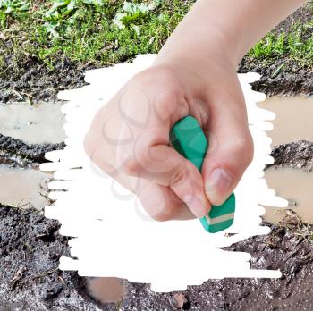 weather concept - hand deletes mud from image of bad country road by rubber eraser