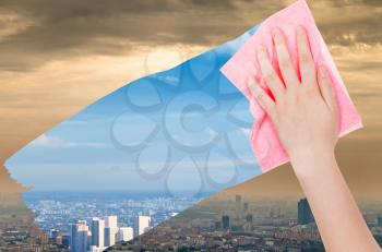 ecology concept - hand deletes smog in city by pink cloth from image and blue cityscape is appearing