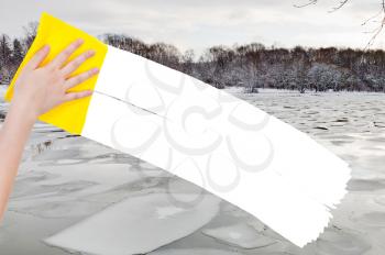 season concept - hand deletes ice blocks in winter river by yellow rag from image and white empty copy space are appearing