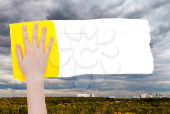 weather concept - hand deletes rainy clouds over town by yellow rag from image and white empty copy space are appearing