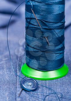 tailoring still life - thread bobbin with needle, button on blue silk cloth