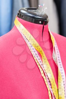 red tailor dummy - mannequin with measure tapes and ready dresses on background
