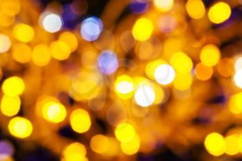 abstract blurred background - dark yellow and violet twinkling Christmas lights bokeh of electric garlands on Xmas tree