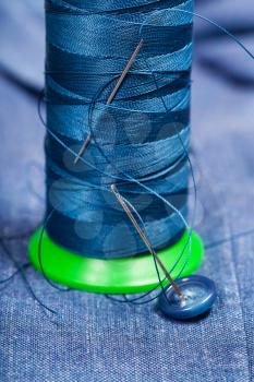 tailoring still life - thread bobbin with needles, button on blue silk textile