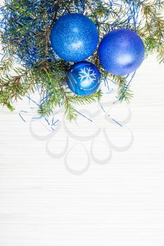 Christmas greeting card - border from three blue Xmas baubles and tree branch on blank paper background