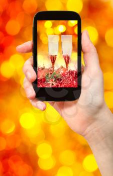 man takes photo of Christmas still life - two glasses of champagne with red and yellow blurred Christmas lights bokeh background