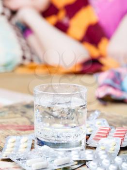glass with medicament and pile of pills on table close up in living room on background